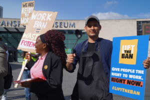 People in work uniforms (a chef's outfit and a business suit_ hold signs saying "lift the ban"