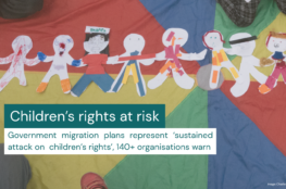 An image of children sitting on colourful rainbow fabric, with a string of paper dolls covering the middle of it