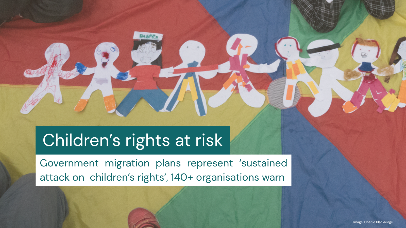 An image of children sitting on colourful rainbow fabric, with a string of paper dolls covering the middle of it